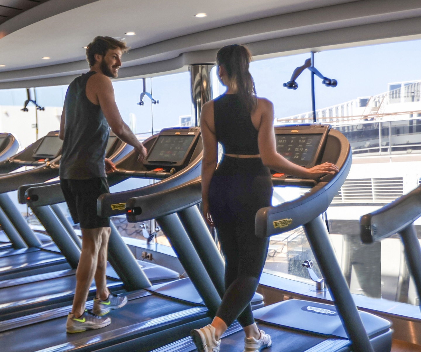 Enjoy a premium fitness experience on MSC Cruises as two individuals work out on treadmills in the well-appointed gym, offering scenic views of the ship and the expansive ocean beyond.