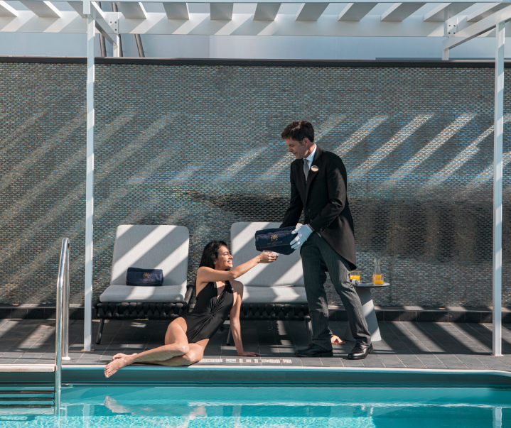 Indulge in the Yacht Club's exclusive Private Solarium on MSC Cruises, where a couple is pampered by a butler, offering personalized service for drinks, food, towels, and more. The image features a crystal-clear, elevated hot tub, epitomizing luxury and relaxation.