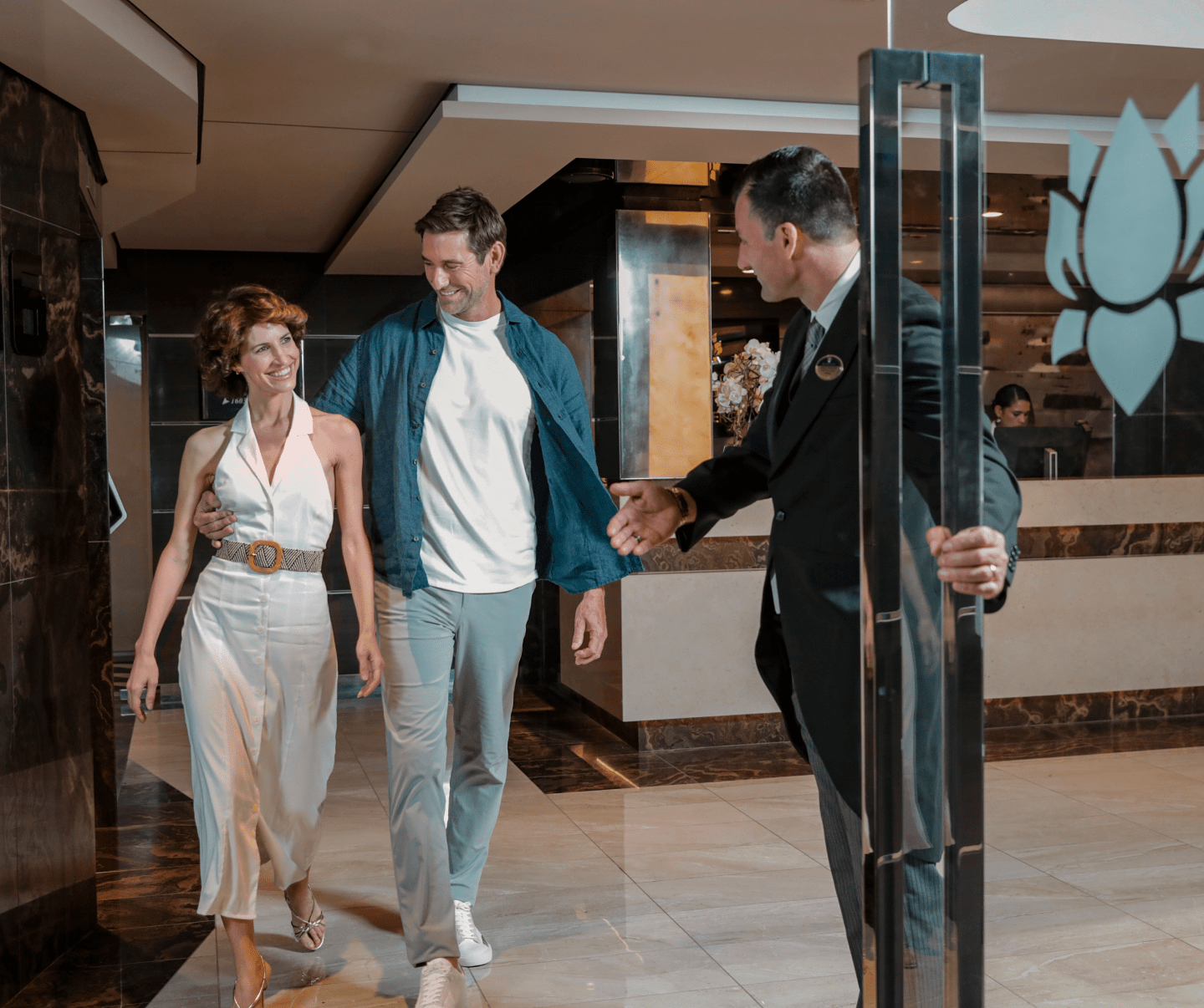 Young couple entering the Yacht Club's front lobby, where they enjoy the perks of luggage delivery and personalized service from the butler, catering to their cruise needs.